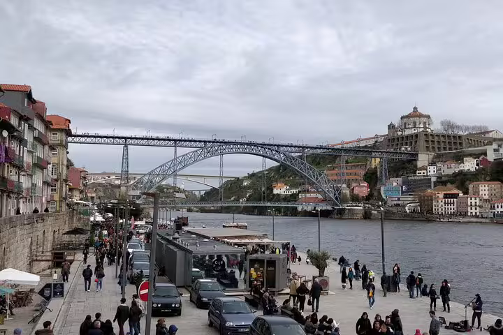 Scenic view of Porto's iconic bridge and riverside, bustling with tourists, part of a private Lisbon to Porto transfer tour.