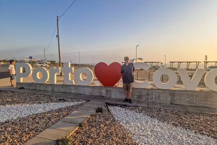 Person standing by the "Porto Covo" sign at sunset, highlighting a scenic stop on the Lisbon to Algarve coastal tour.