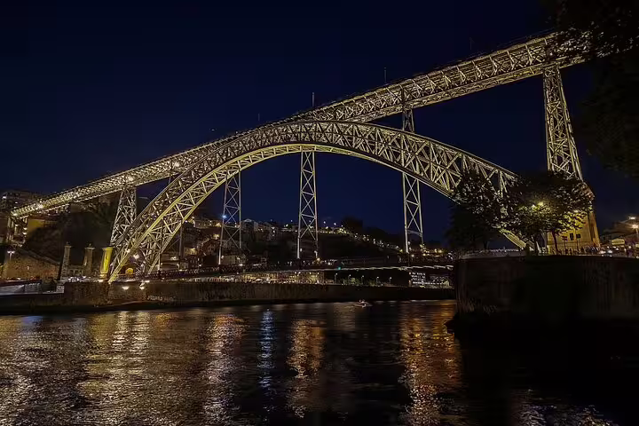 Night view of Porto's iconic Dom Luís I Bridge illuminated over the Douro River, a highlight of the Lisbon to Porto tour.