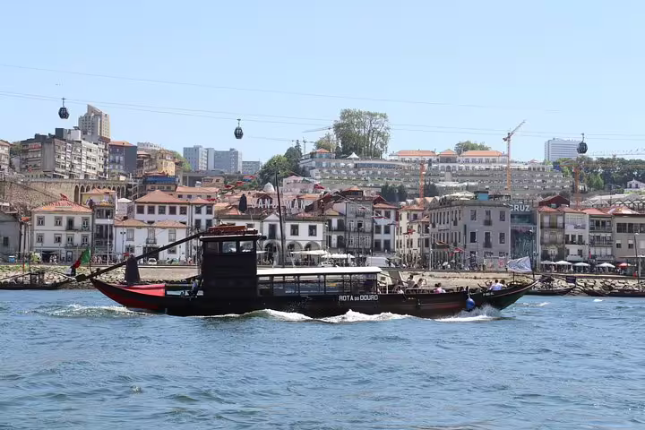 Scenic view of a traditional boat cruising on the Douro River with Porto's historic waterfront in the background.