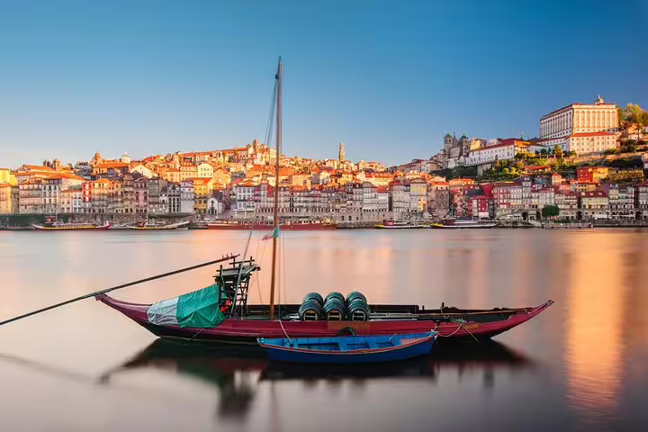 Scenic view of a traditional boat on the Douro River against Porto's historic skyline at sunset.