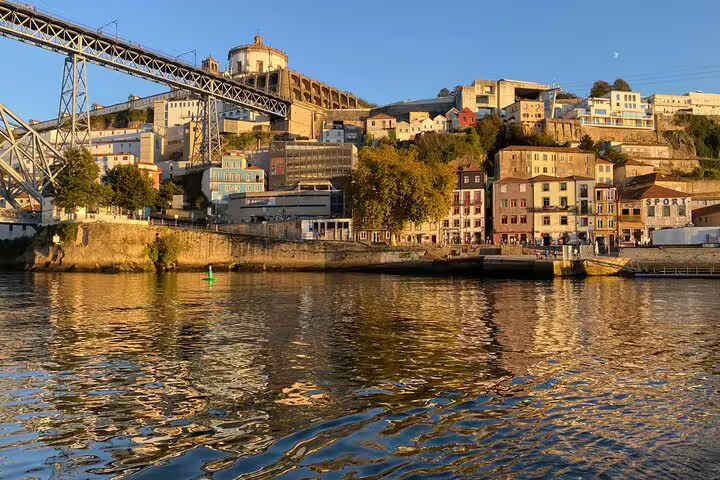 Scenic view of Porto's historic Ribeira district from the Douro River, highlighting colorful buildings under a golden sunset.