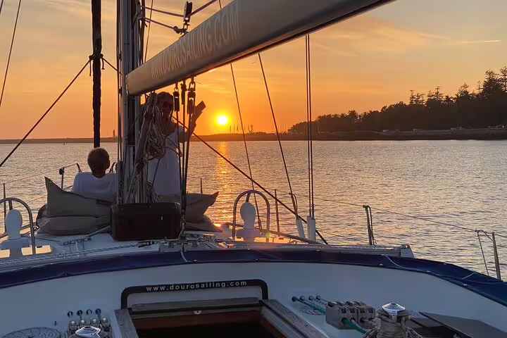 Sunset view from a boat on the Douro River in Porto, featuring relaxing passengers enjoying wine and snacks on a scenic tour.