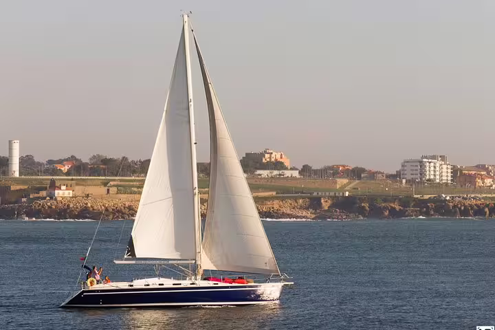 Sailboat cruising the Douro River in Porto with scenic views, offering a delightful tour experience with wine and snacks.