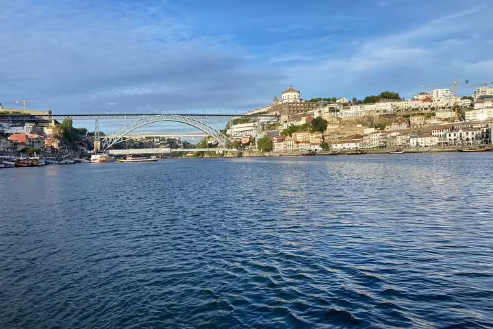 Scenic view of Porto's Douro River with iconic bridge, perfect for a relaxing boat tour with wine and snacks included.