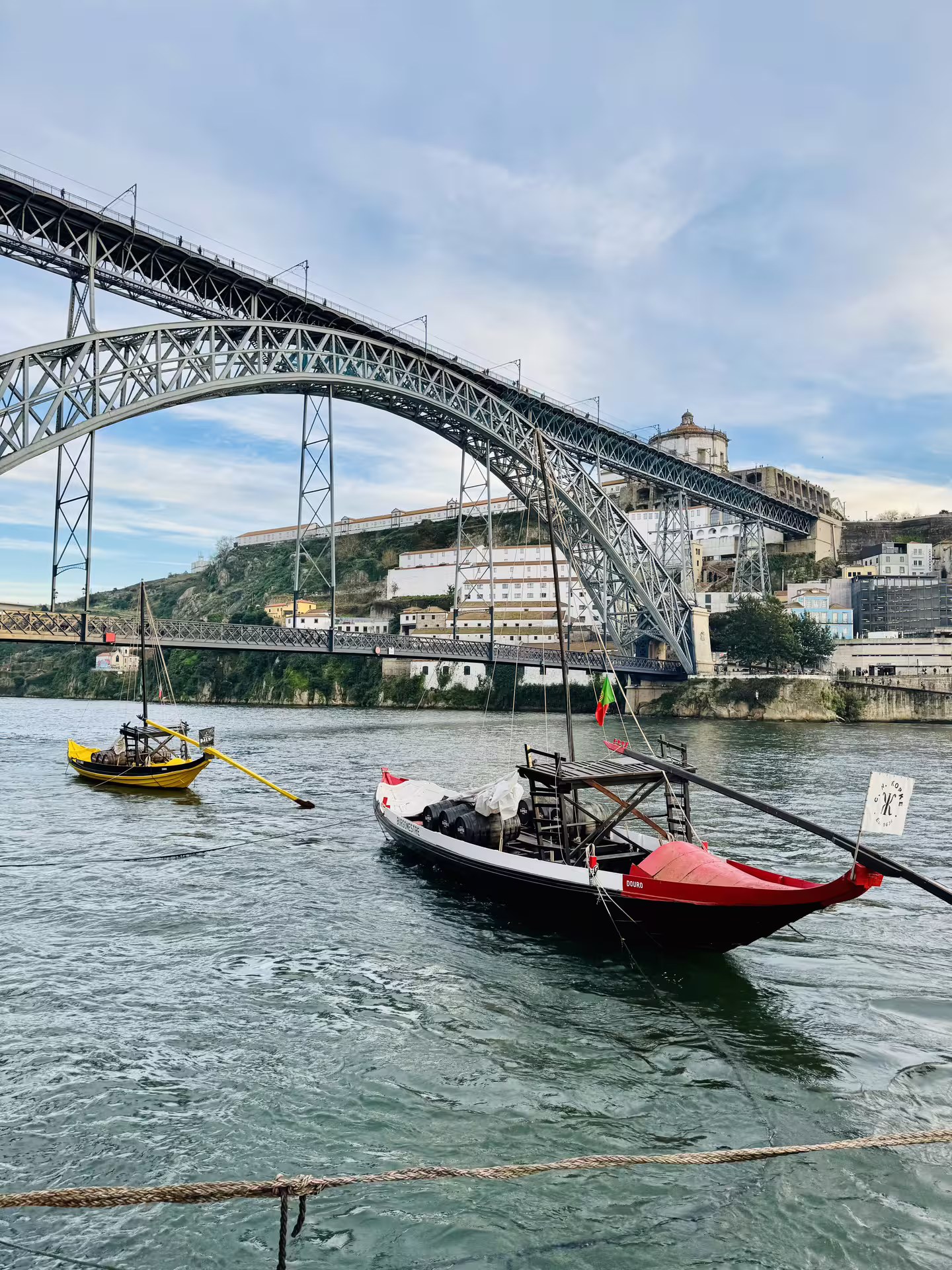 Traditional boats on the Douro River with iconic Dom Luís I Bridge in Porto's historic center, perfect for a scenic walking tour.