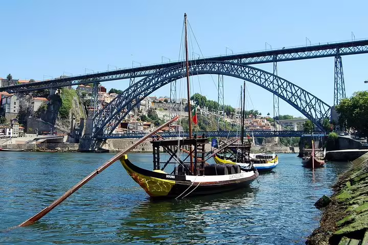 Traditional rabelo boats float on the Douro River with the iconic Dom Luís I Bridge in Porto, ideal for river cruises.