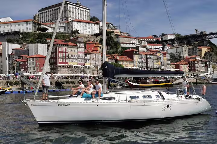 Tourists relaxing on a sailboat cruising past Porto's historic Ribeira district during a scenic Douro River tour.