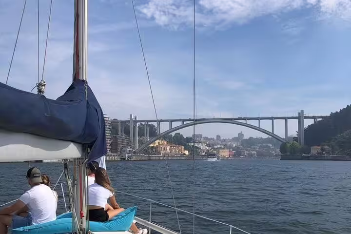 Sailing under the iconic Arrábida Bridge on a sunny Douro River tour, showcasing Porto's stunning waterfront landscape.