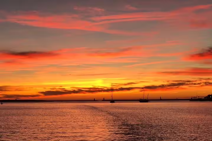 Vibrant sunset over the Douro River with silhouettes of sailboats, perfect for a romantic private tour experience.