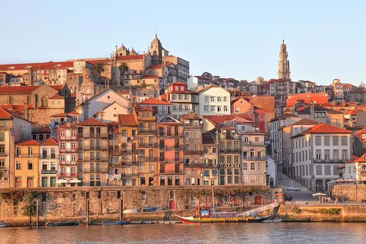 Colorful historic buildings and traditional boats along Porto's Douro River at sunset, viewable on a private tour from Lisbon.