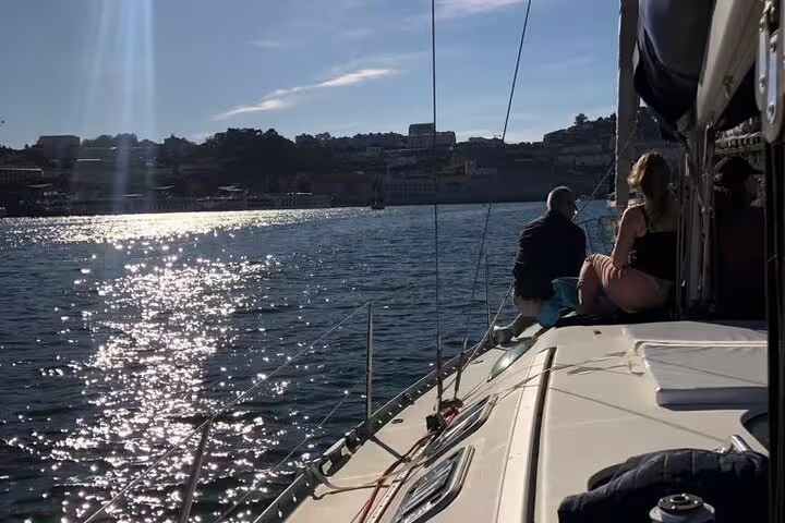 Passengers admire the sunset from a yacht on the Douro River, with the Porto skyline in the distance.