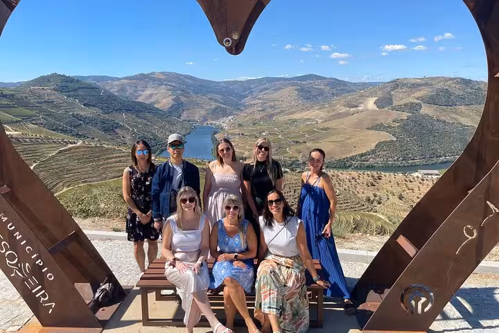 Happy group at Douro Valley miradouro framed by heart art, overlooking terraced vineyards on a Porto wine regions tour.