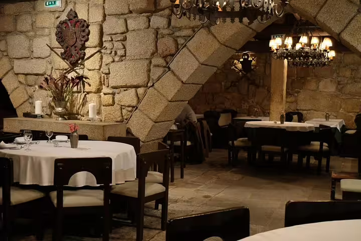 Cozy stone-walled restaurant in Porto set for an intimate Fado dinner, featuring elegant chandeliers and white tablecloths.