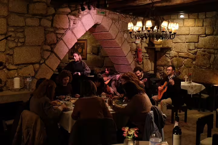 Cozy Porto restaurant with stone walls, guests dining, and live Fado music, perfect for a moonlit walk and cultural evening.