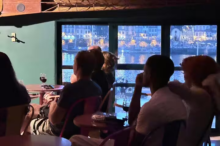 People enjoying authentic Fado music at a cozy riverside venue in Porto, with scenic views of the illuminated riverfront.