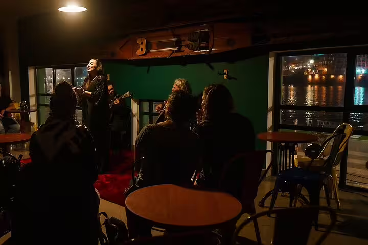 Intimate Fado performance by the Porto riverfront with a soulful singer, cozy ambiance, and scenic nighttime view.