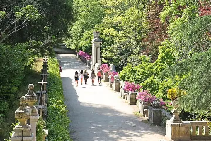 Visitors strolling through a lush, flower-lined path in Coimbra's gardens, featured in the Porto to Fátima full day tour.