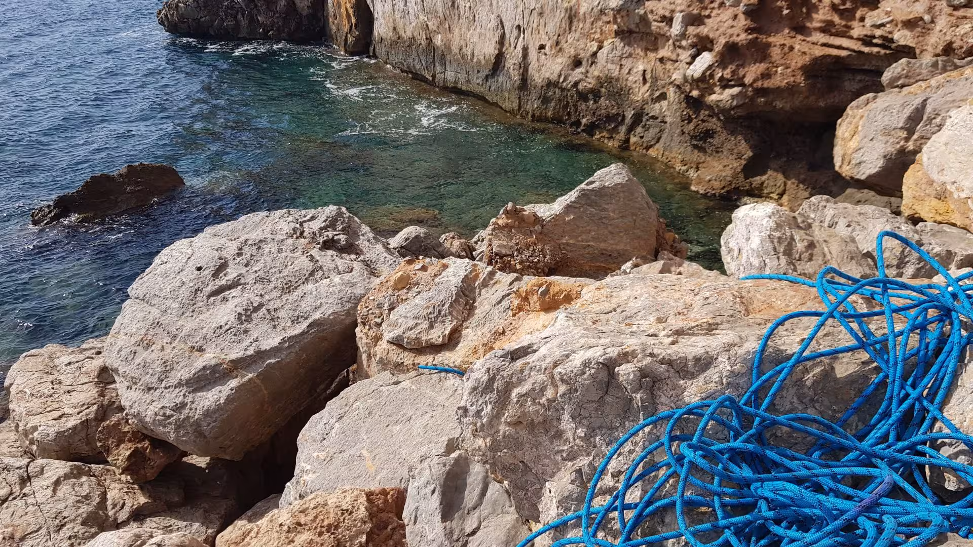 View of the rocky coastline at Porto Flavia with blue climbing rope ready for dry canyoning adventure.