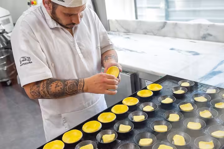 Baker prepares traditional custard tarts in Porto kitchen during popular food tour.