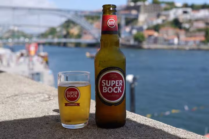 Enjoy a refreshing Super Bock beer with a scenic view of Porto's Douro River on a sunny day.