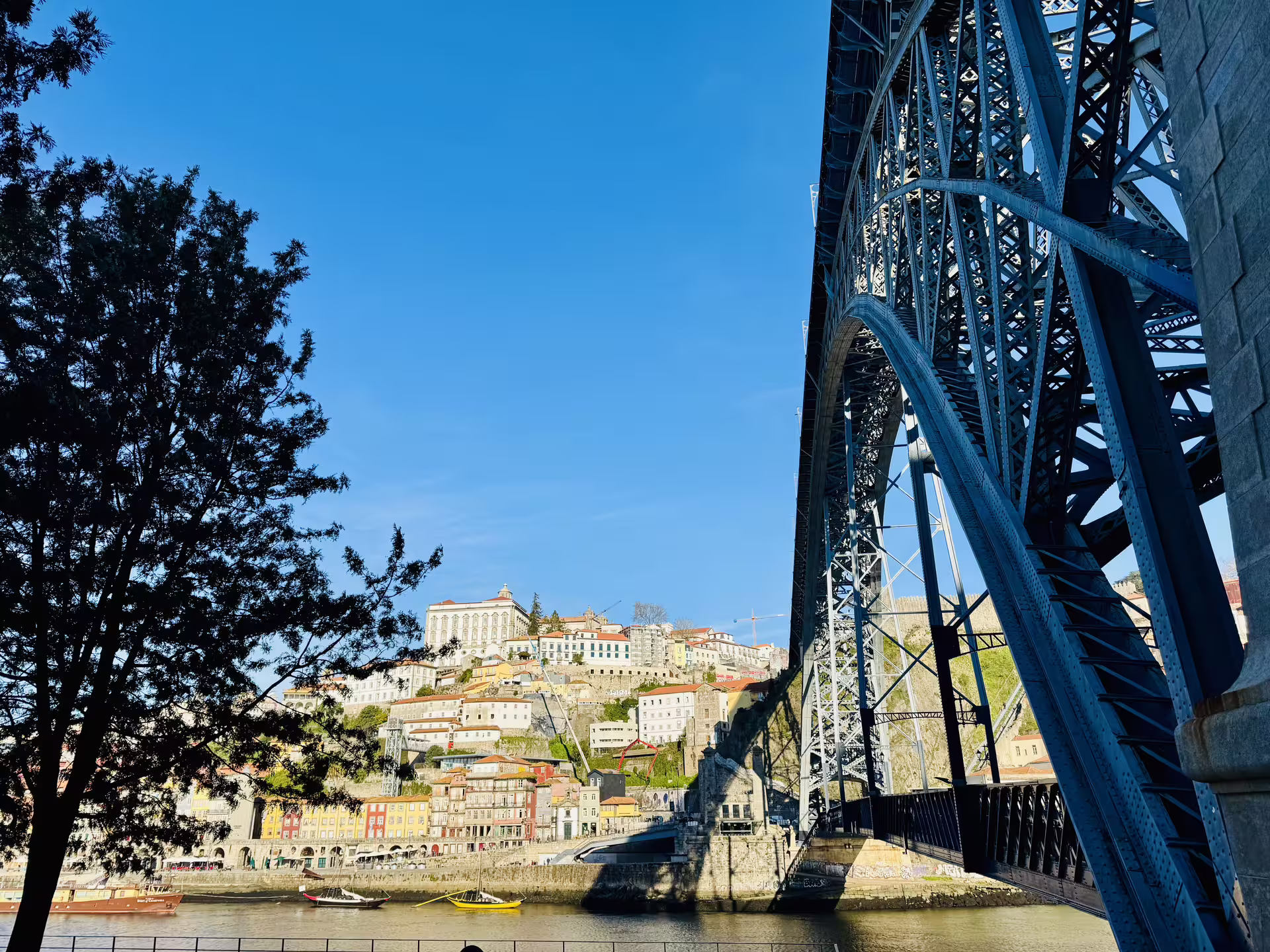 View of Porto's colorful hillside buildings and the iconic Dom Luís I Bridge spanning the Douro River under a clear blue sky.