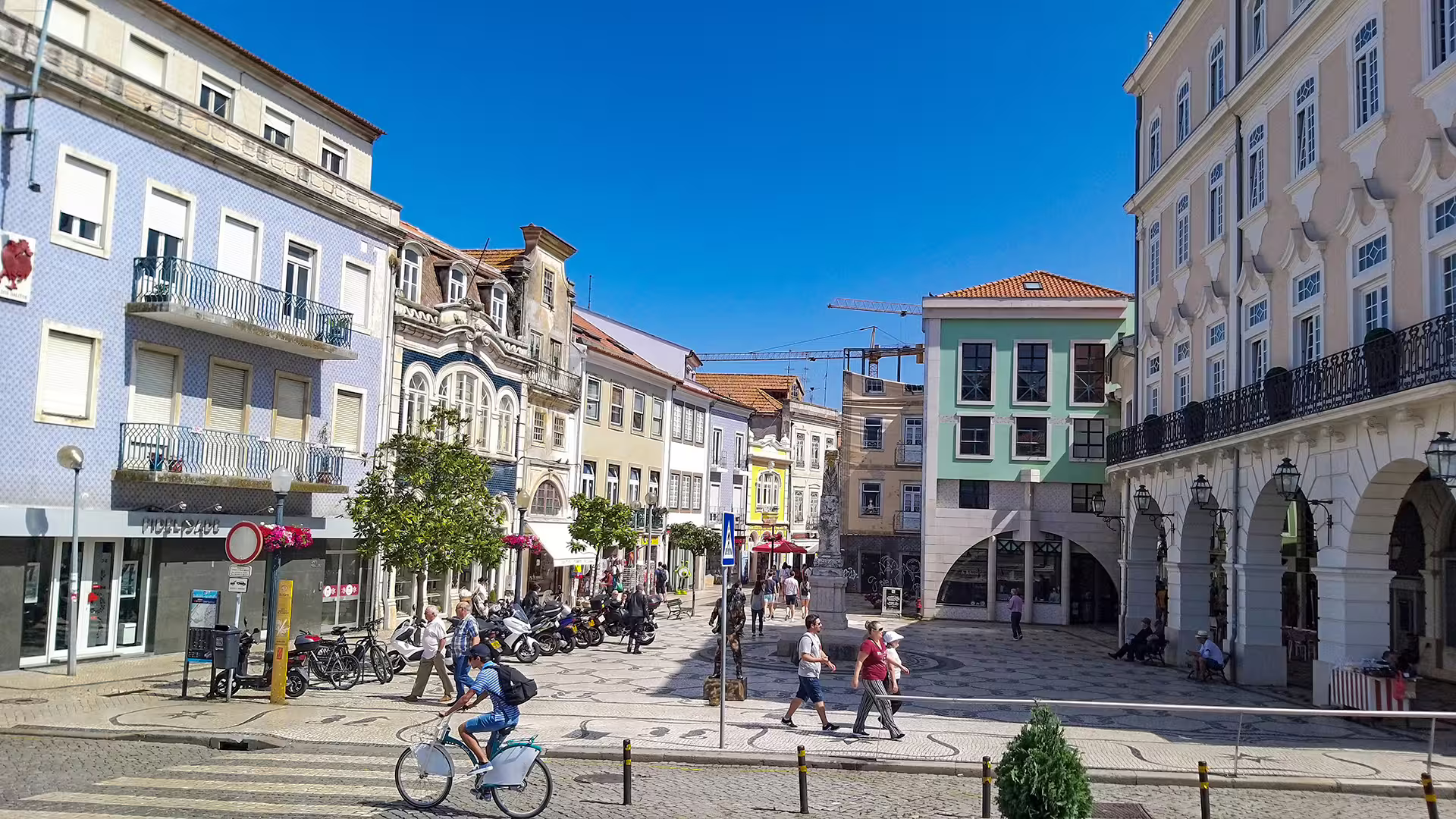 Charming Portuguese plaza with vibrant buildings and pedestrians in a sunny square, ideal for a custom Porto to Lisbon tour.