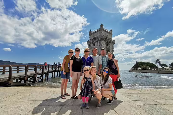 Group of tourists enjoying a sunny day by the iconic Belém Tower in Lisbon during a Porto to Lisbon transfer tour with stops.