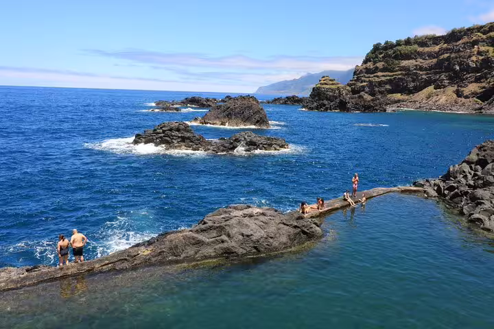 Scenic view of natural rock pools with tourists enjoying the clear blue waters at Porto Moniz, perfect for a 4x4 Jeep tour adventure.
