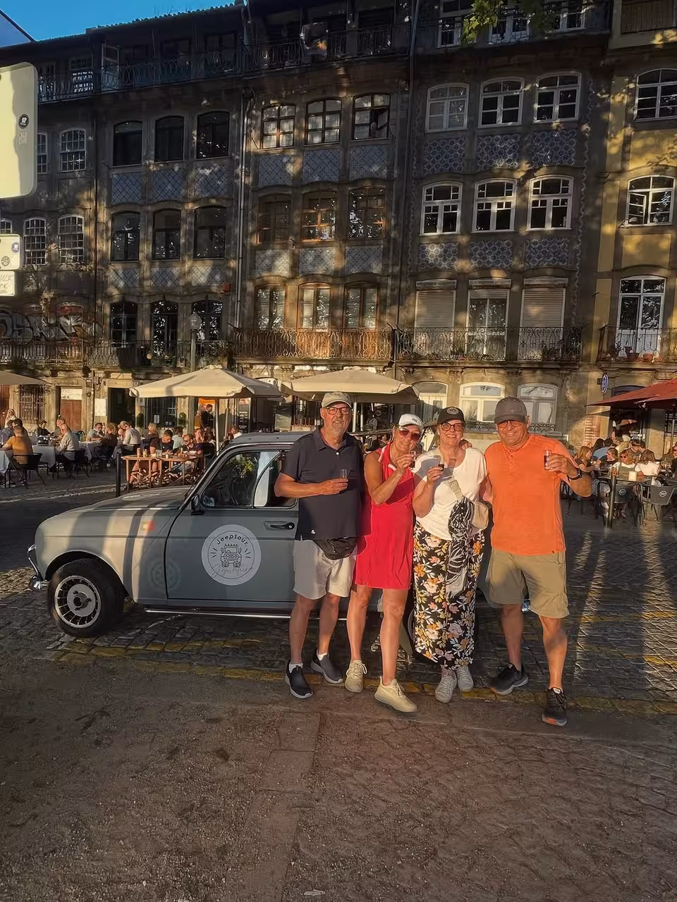 Friends enjoying Porto by Night classic car tour, sipping port wine in Ribeira square with azulejo facades