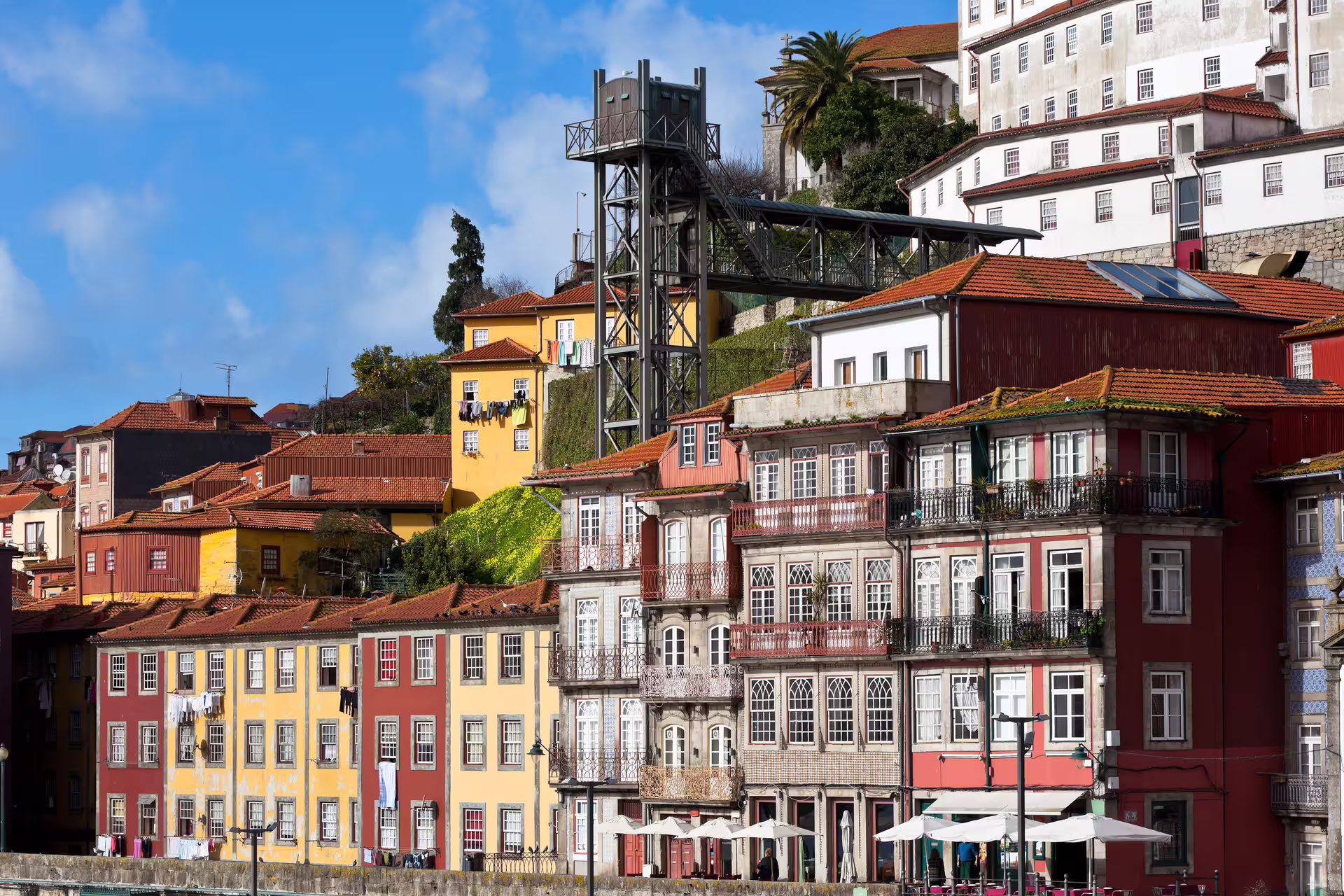 Colorful historic buildings in Porto's old town with a modern elevator, vibrant facades, and blue sky, ideal for a walking tour.