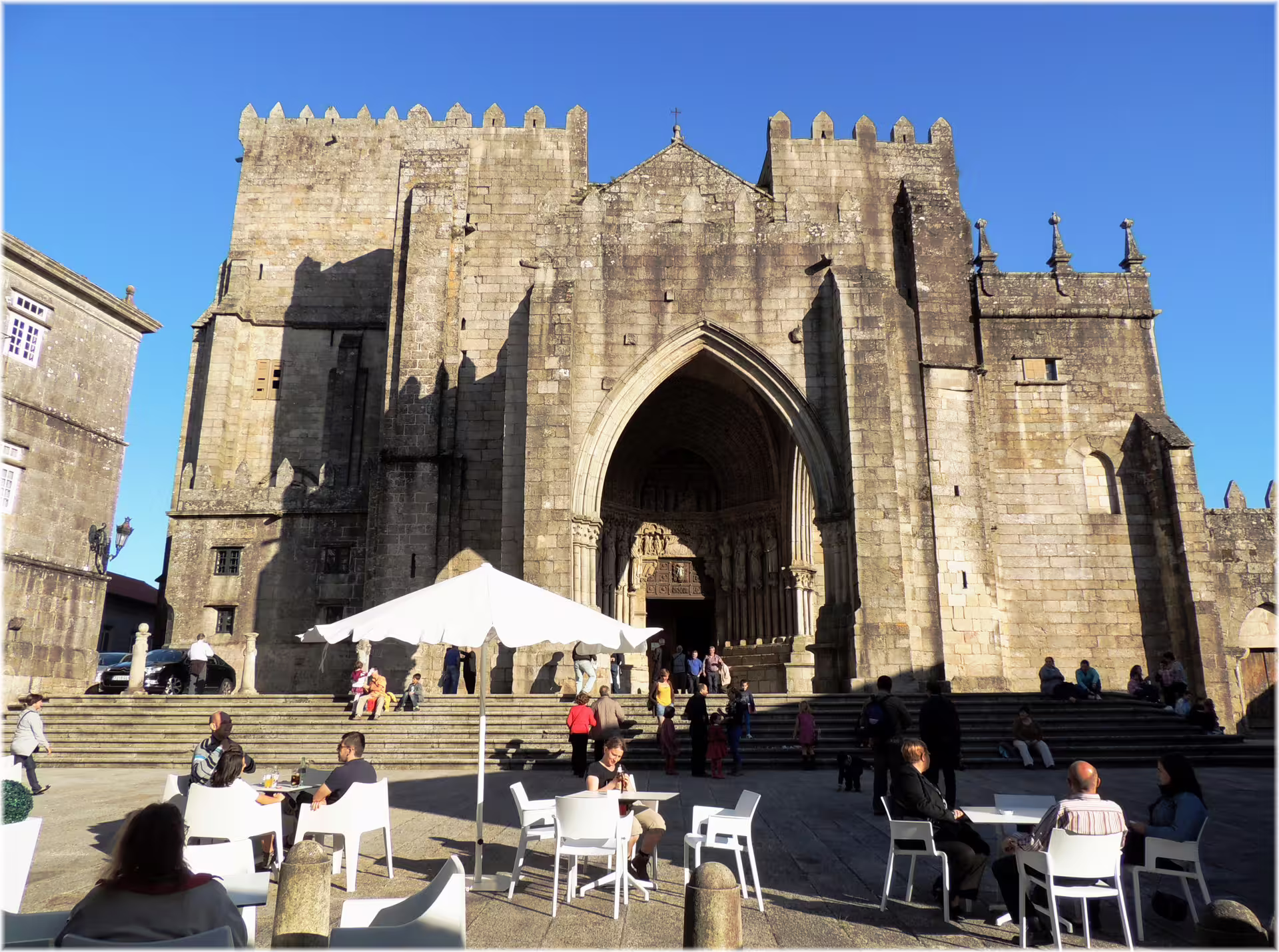 Sunlit entrance of a medieval cathedral in Pontevedra, with tourists enjoying an outdoor café setting.
