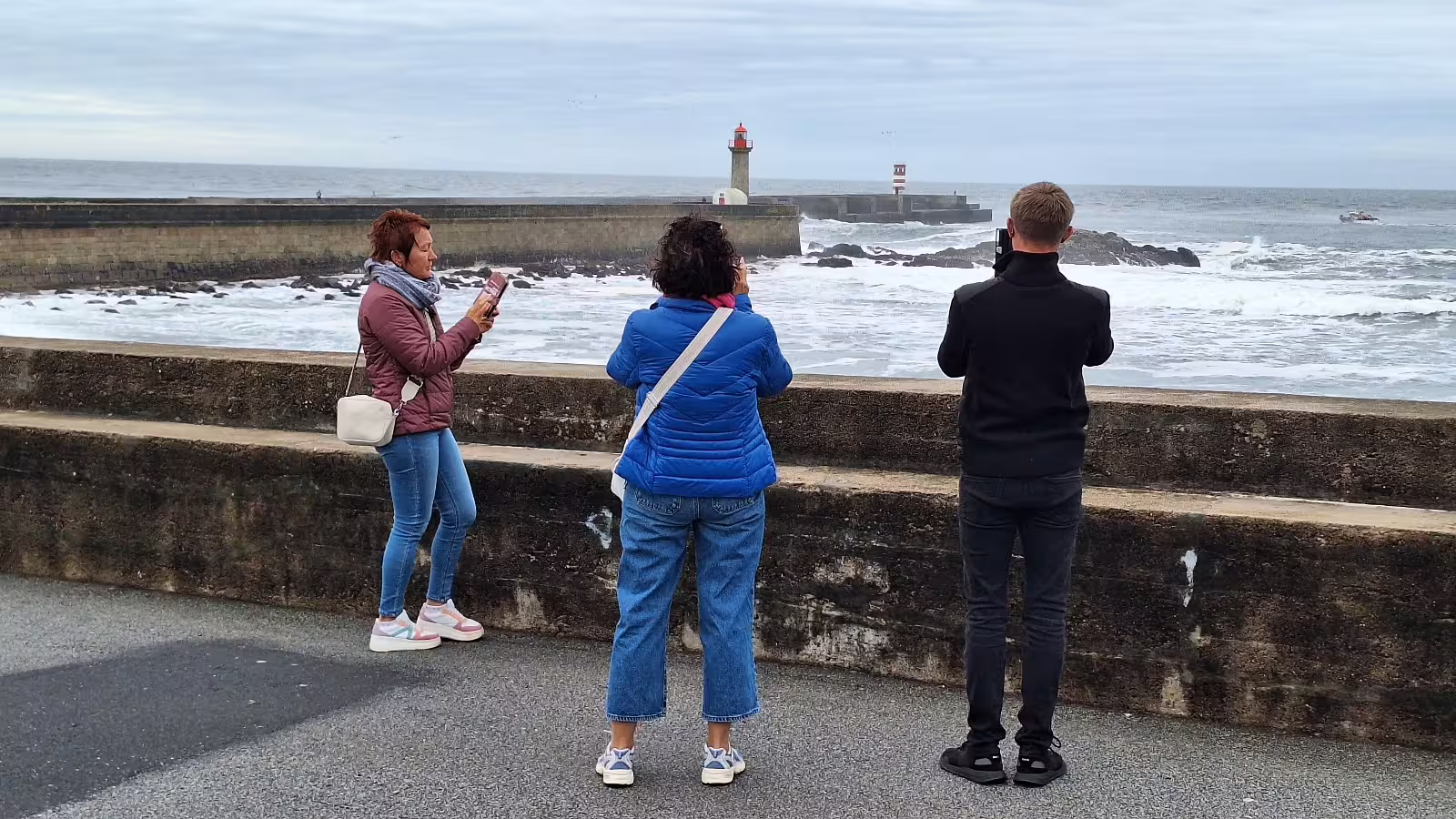 Tourists capturing the scenic Porto coastline and iconic lighthouse during a private afternoon tour with local experts.