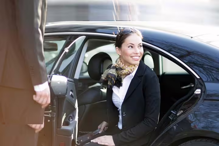 Smiling woman exits luxury car, greeted by a driver, showcasing private airport transfer service in Porto.