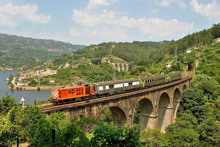 Scenic train journey over a historic bridge surrounded by lush hills on a Porto to Régua day trip.