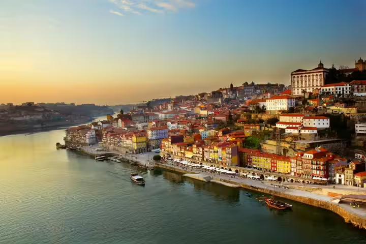 Scenic view of Porto's historic Ribeira district at sunset, featuring colorful buildings along the Douro River in northern Portugal.