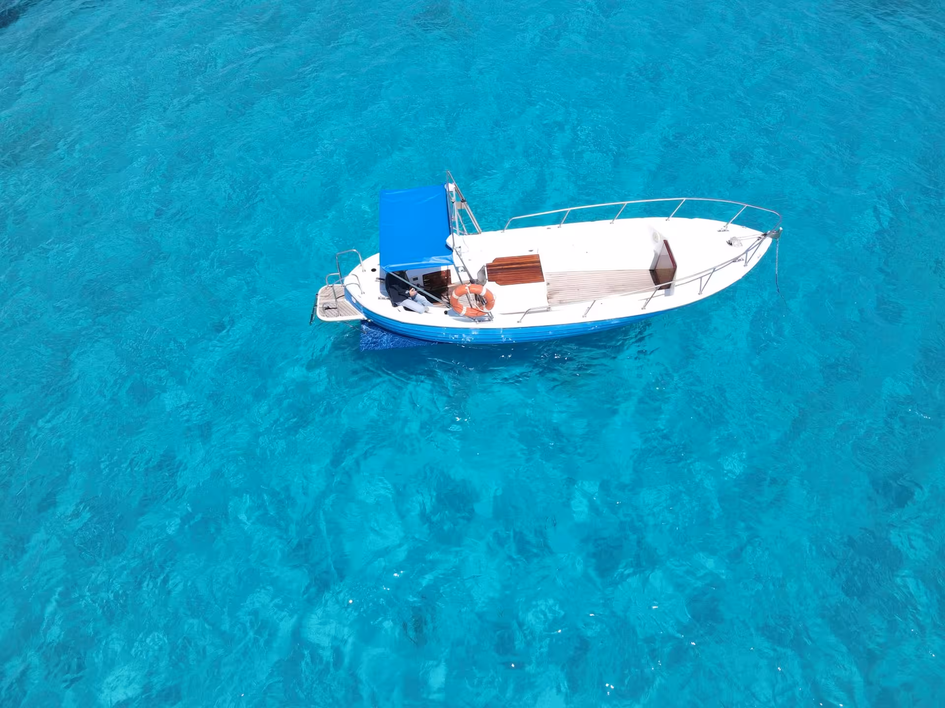 Pristine blue boat floating on crystal-clear waters near Golfo Aranci, offering a serene Sardinian boat tour experience.