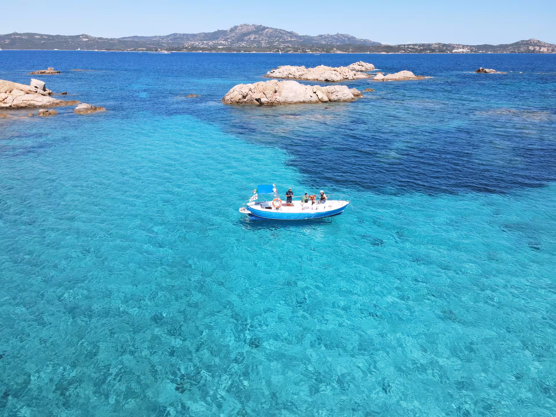 Small boat with tourists exploring clear turquoise waters near Porto Rotondo, Sardinia's stunning coastline in view.