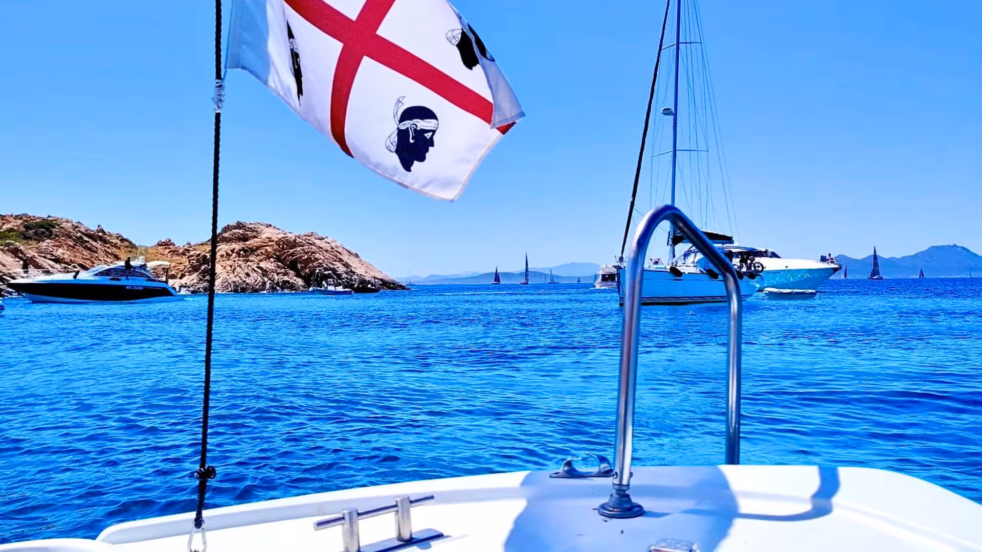 Scenic view from a boat in Porto Rotondo with Sardinian flag, yachts, and clear blue waters in the background.