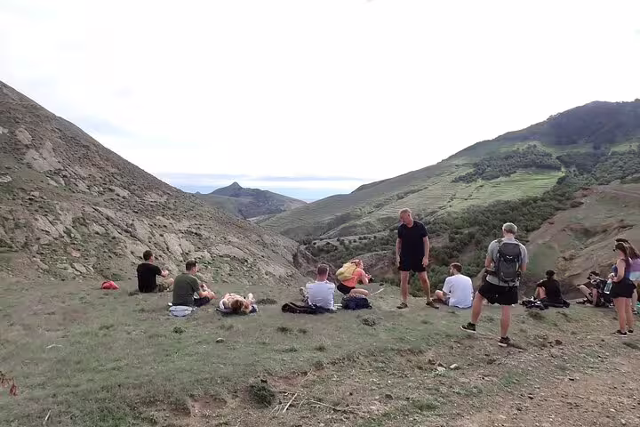 Hikers rest on scenic Pico Branco & Terra Chã trail, surrounded by lush hills and ocean views, perfect for nature enthusiasts.