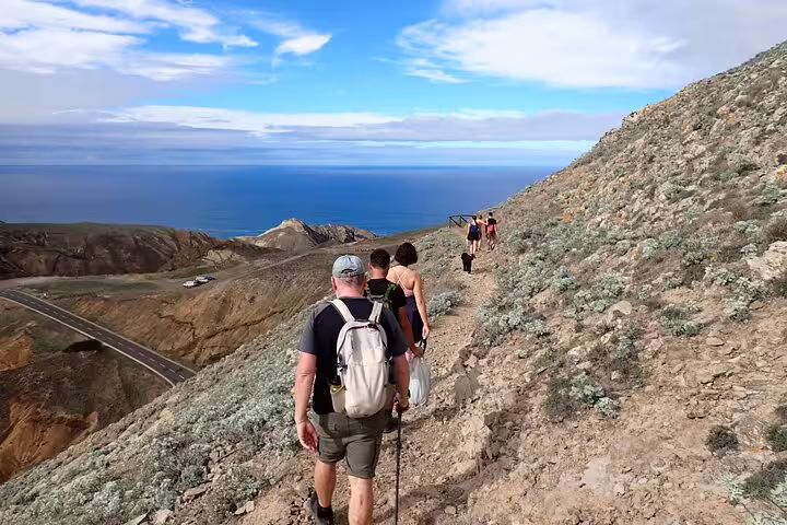 Hikers traverse a scenic coastal trail on the Pico Branco & Terra Chã tour, with stunning ocean views under a vibrant sky.