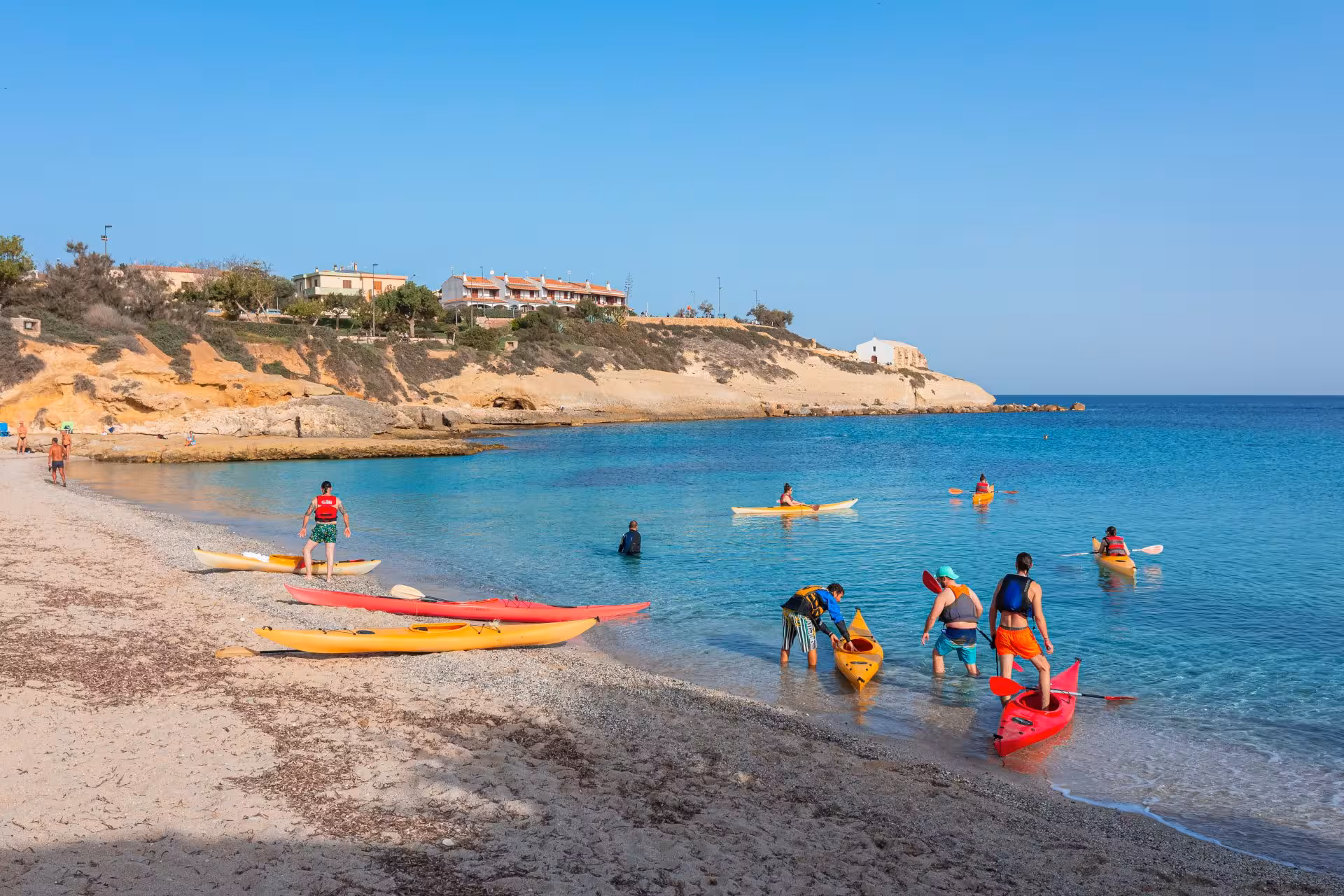 Group of people preparing kayaks on the sandy beach for an exciting excursion in Porto Torres' blue waters.
