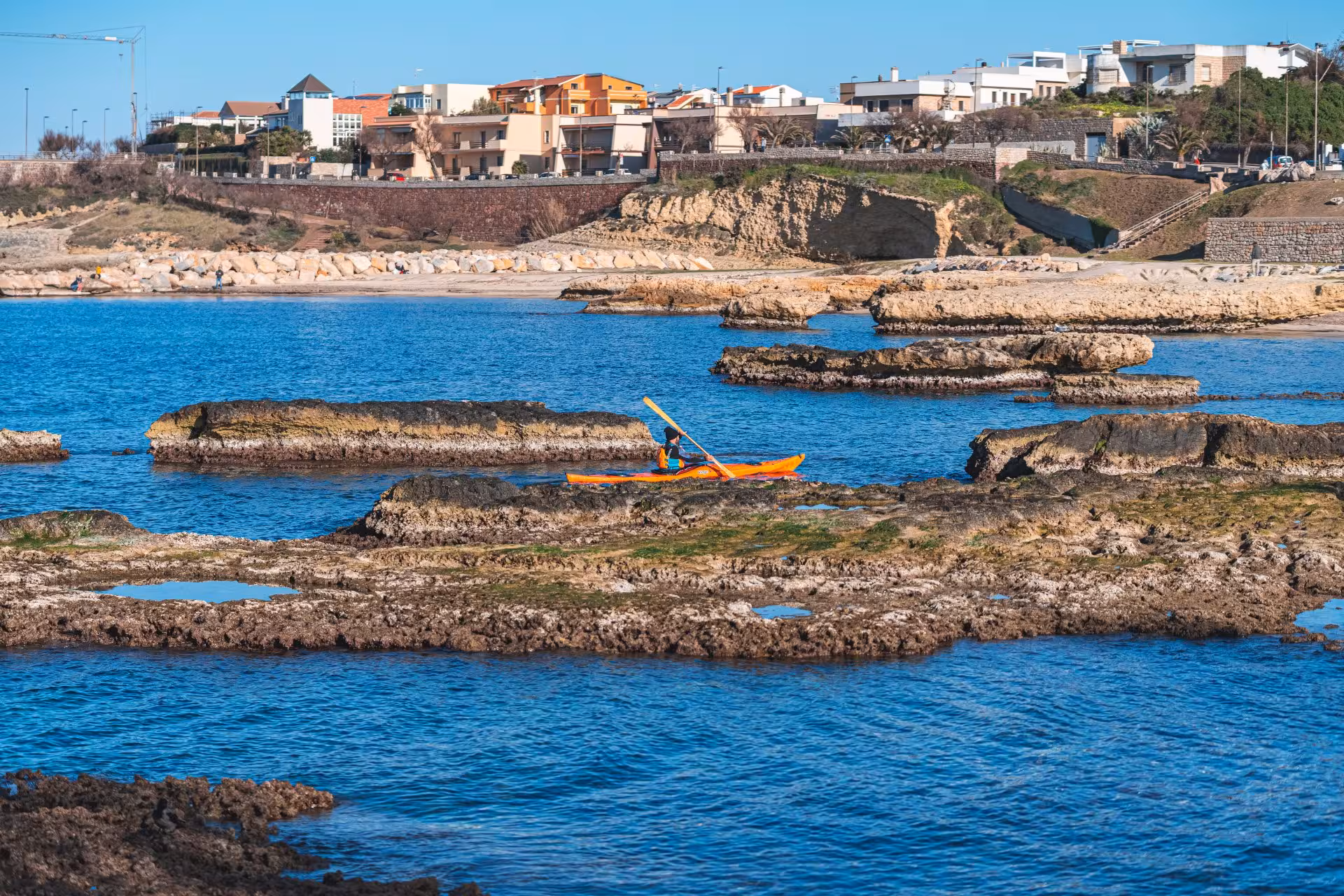 Kayaker navigating through rugged coastal landscapes of Porto Torres, ideal for scenic adventure tours.