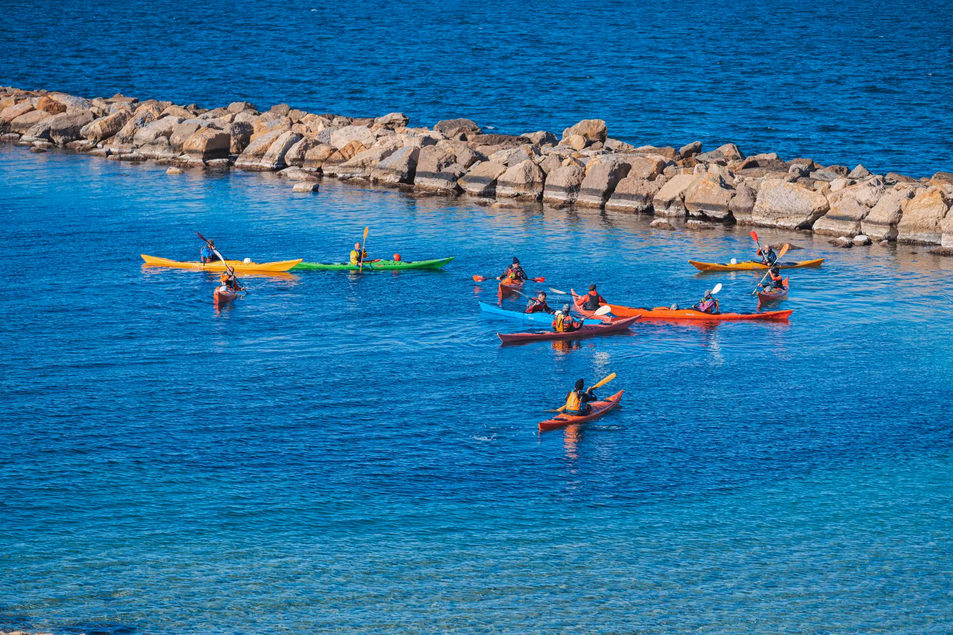 Group enjoying a colorful kayak excursion in the clear blue waters of Porto Torres, perfect for adventure seekers.