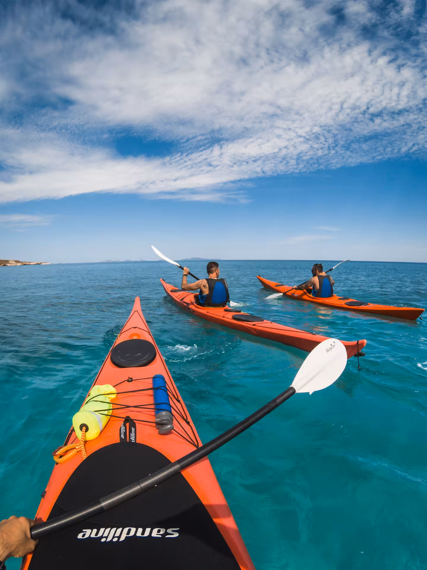 Two kayakers paddling in crystal-clear waters under a blue sky in Porto Torres, offering an idyllic adventure experience.