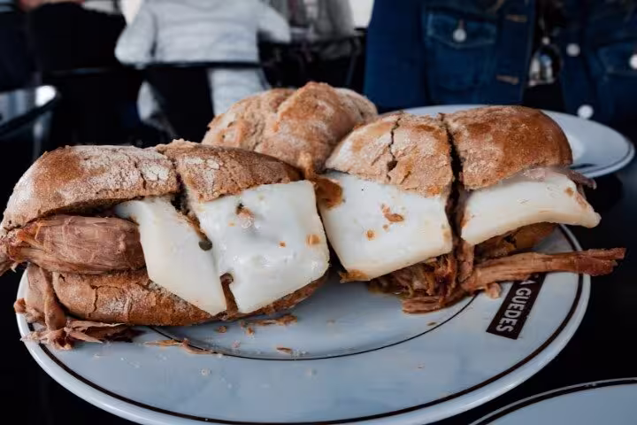 Traditional Porto sandwich with juicy pork and melted cheese on a rustic plate, perfect for a Porto food tour.