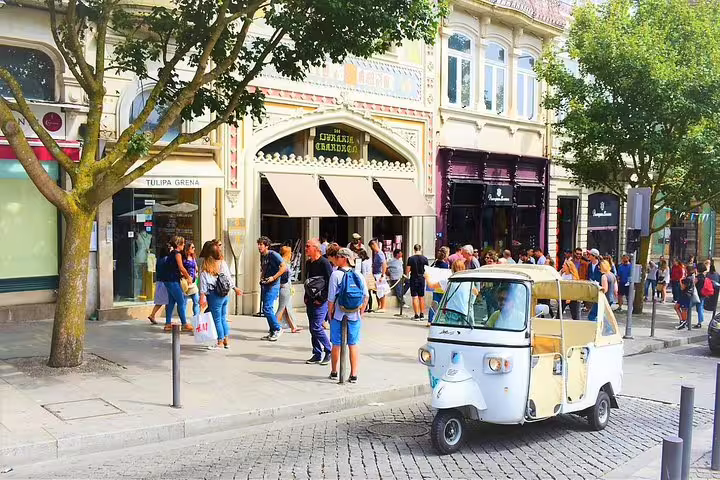 White tuk tuk parked in front of the historic Livraria Lello in Porto, with tourists exploring the vibrant street scene.