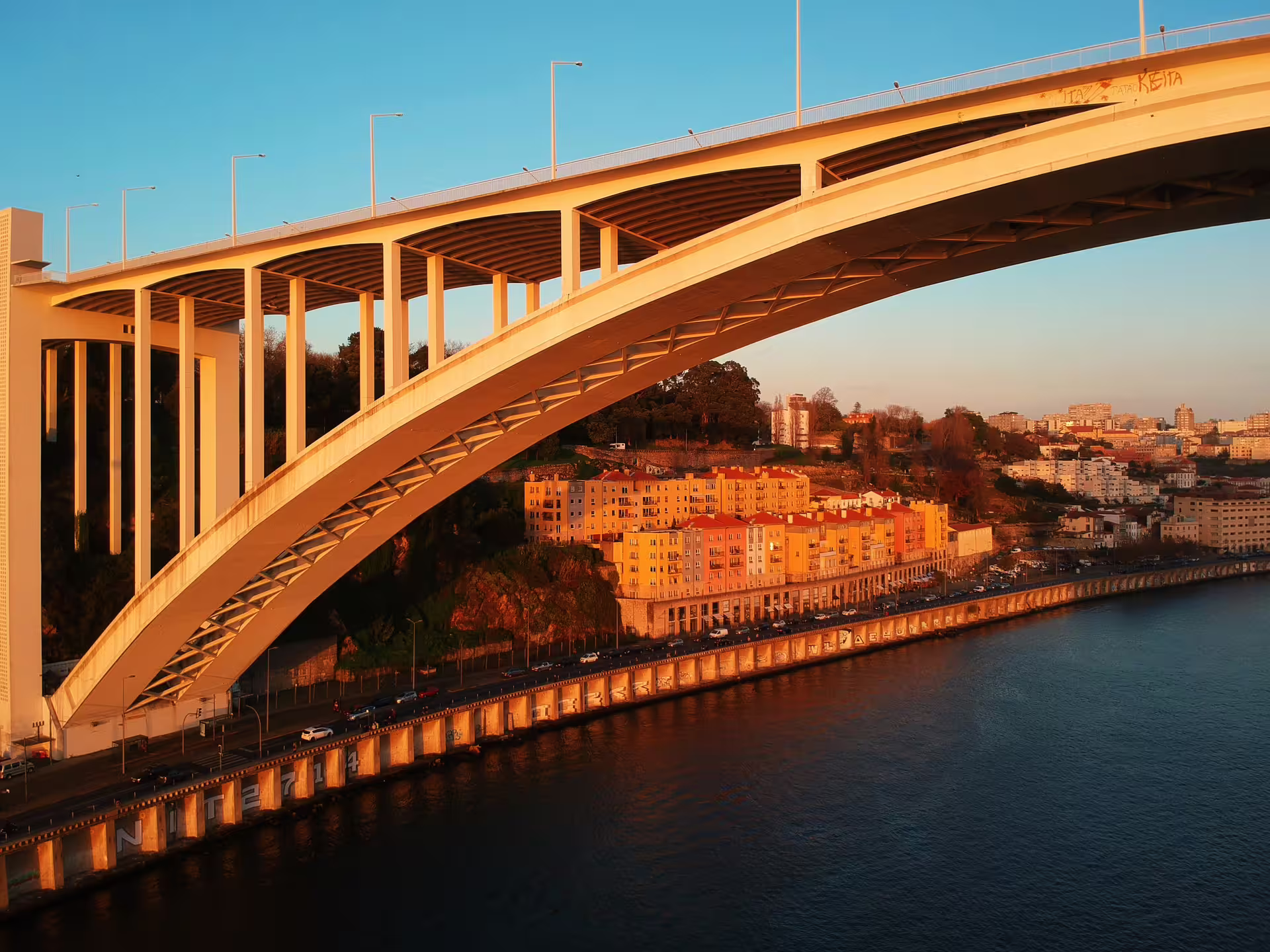 Sunset view of Porto's Arrábida Bridge and riverside buildings, highlighting scenic routes on a guided tuk tuk tour.