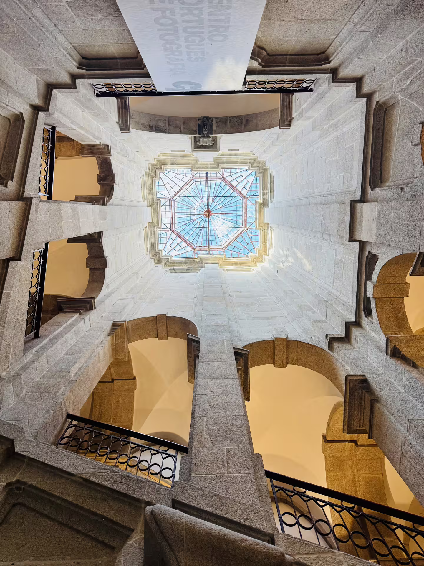 Looking up at a stunning glass ceiling inside a historic building in Porto, showcasing intricate architecture on a walking tour.