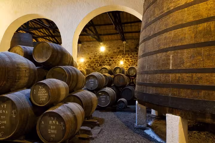 Traditional wine barrels aging in a dimly lit cellar in Porto, highlighting Portugal's wine culture.